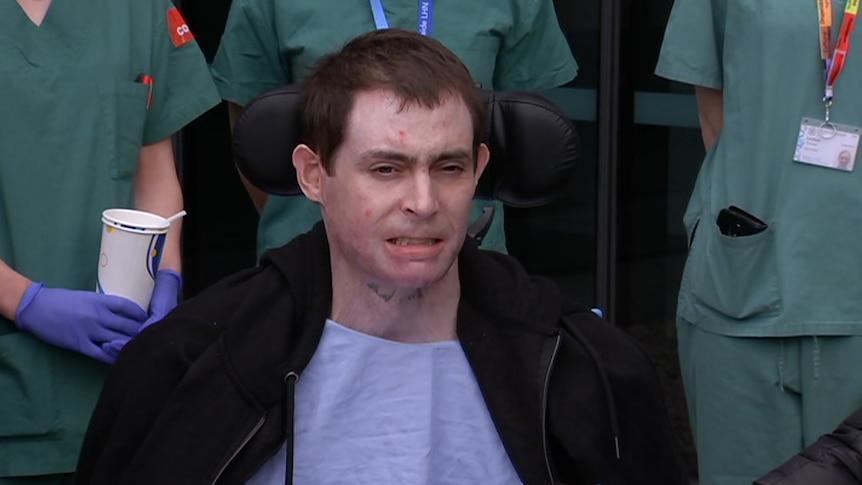 Glenn Ogg sits in a wheelchair with hospital staff surrounding him