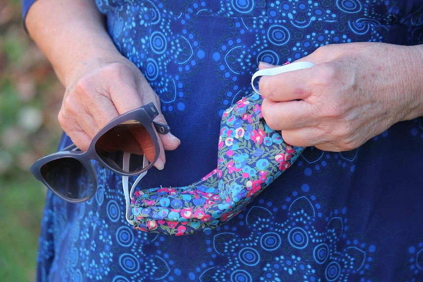 Close up of Nancy Sommerfield's hands holding her sunglasses and her colourful printed home made face mask