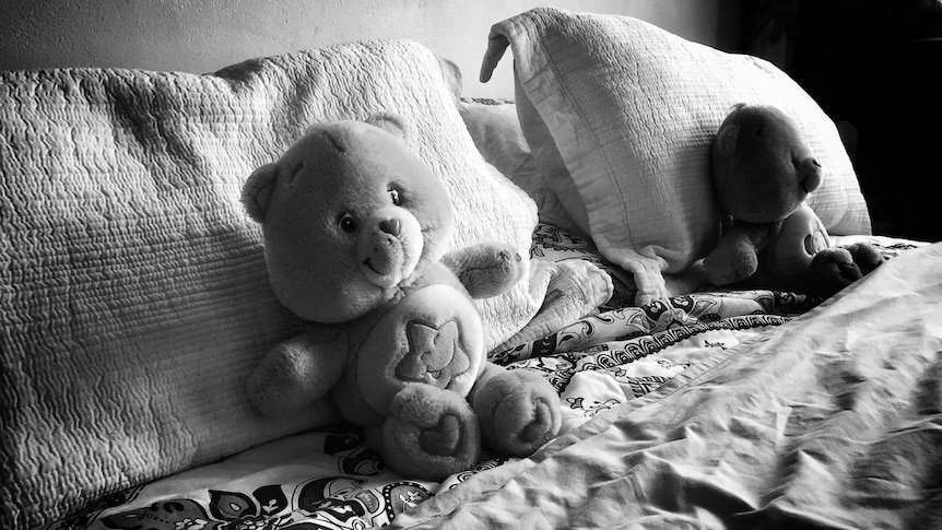 Two teddy bears sit on a bed.