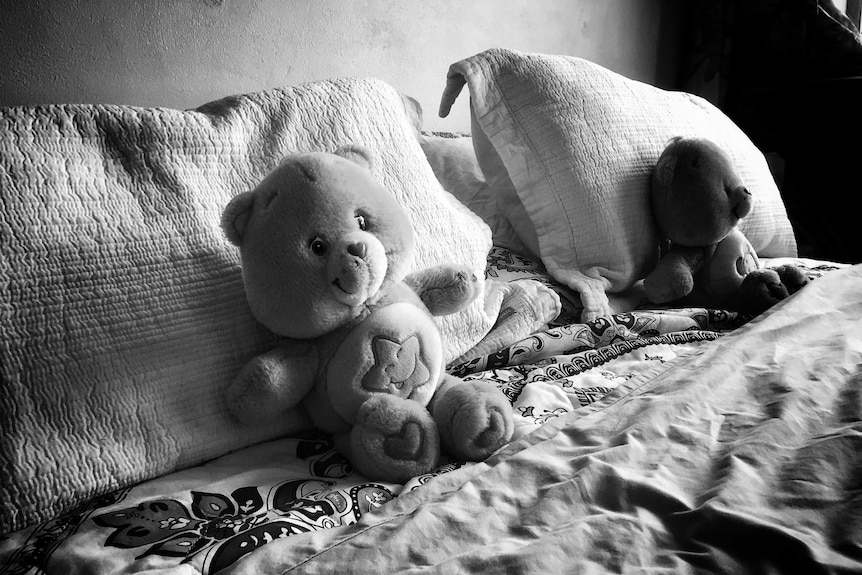 Two teddy bears sit on a bed.