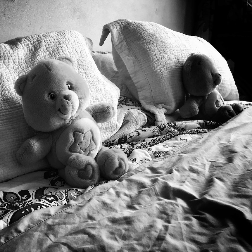 Two teddy bears sit on a bed.