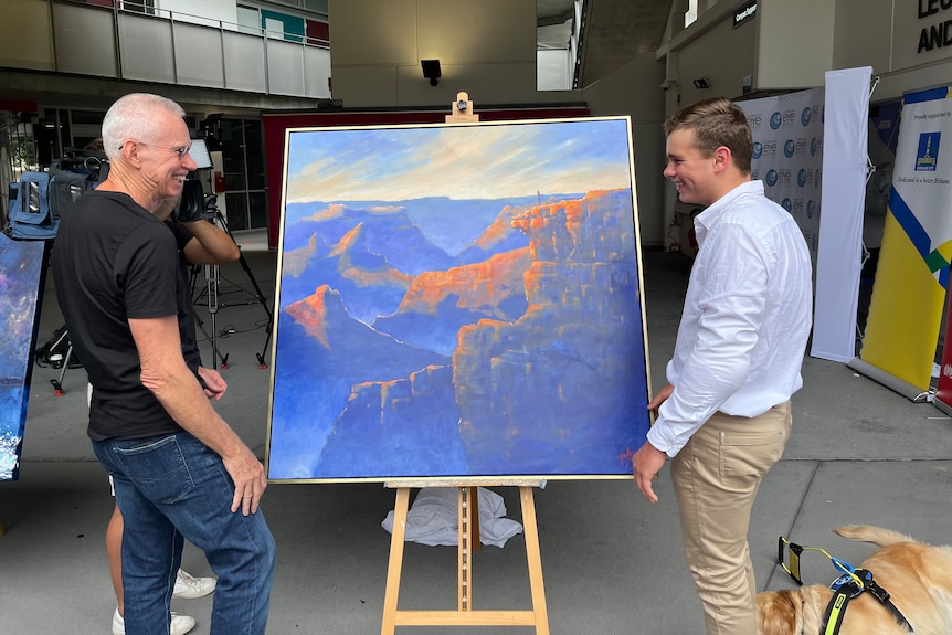Two men standing next to a painting smiling.