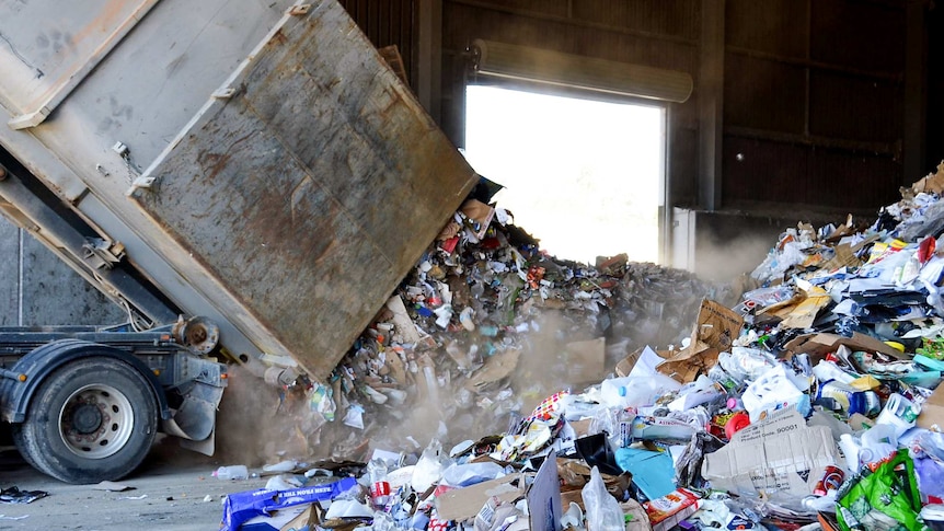 Truck tipping recyclable items at recycling plant.