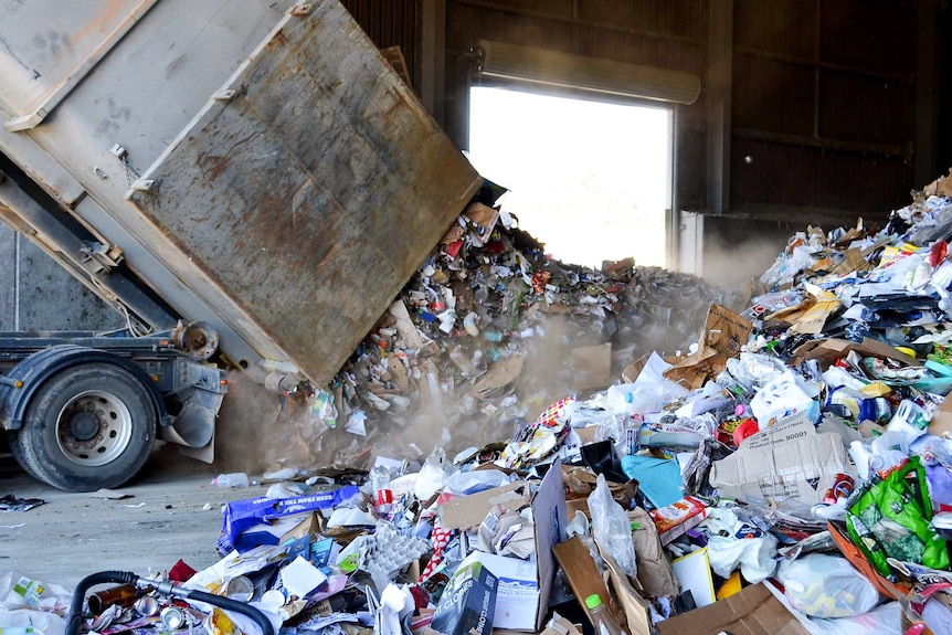 Truck tipping recyclable items at recycling plant.