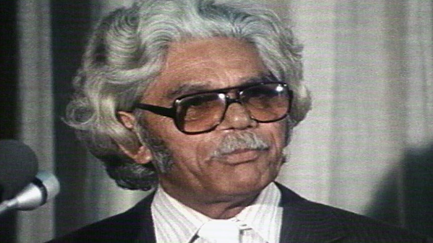 A head and shoulder shot of Neville Bonner wearing glasses and a pin-striped suit.