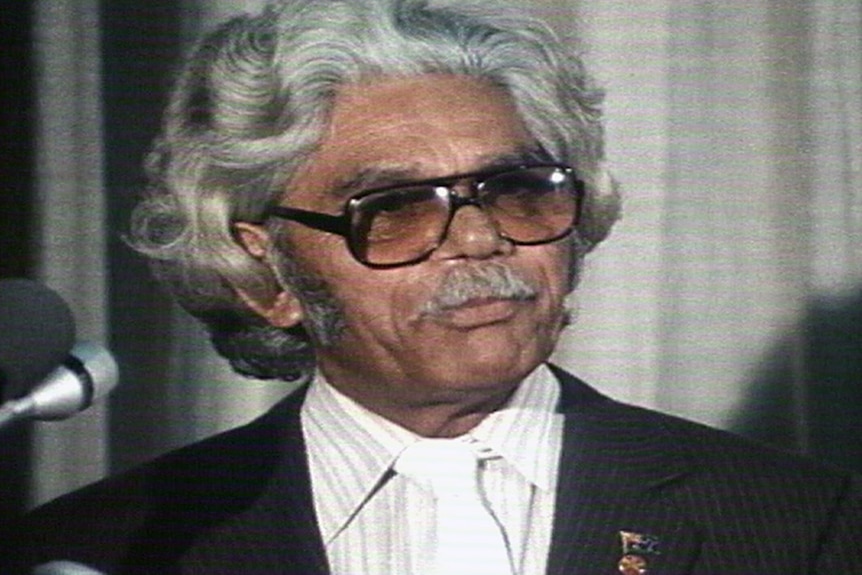 A head and shoulder shot of Neville Bonner wearing glasses and a pin-striped suit.