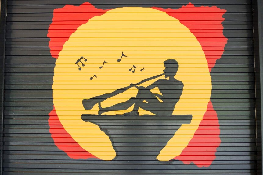 A silhouette painting incorporating the Aboriginal flag with a man playing a didgeridoo in the yellow section.