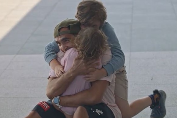 Eddie Betts sits on the ground and hugs three of his small children. Everyone is very happy