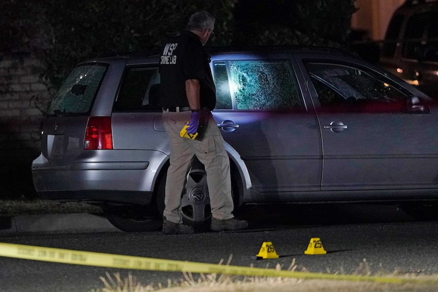 A police officer shines a torch on the broken window of a car after US Marshals shot dead suspected killer Michael Reinoehl.