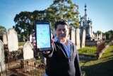A woman holding Google Maps up, directing herself to a grave stone in Rookwood Cemetery.