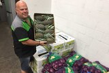 Man holds box of pineapples, near bag of onions at Sydney Markets