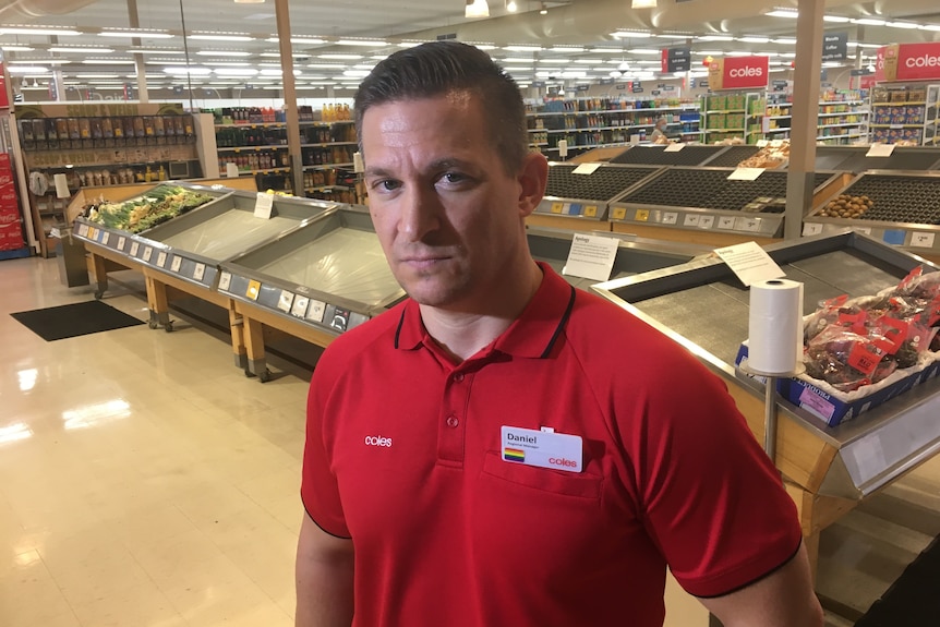 a man in a red collared shirt stands inside a supermarket with empty shelves
