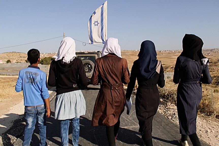 Four teenagers from the village of Tuba walk to school accompanied by an armoured vehicle.