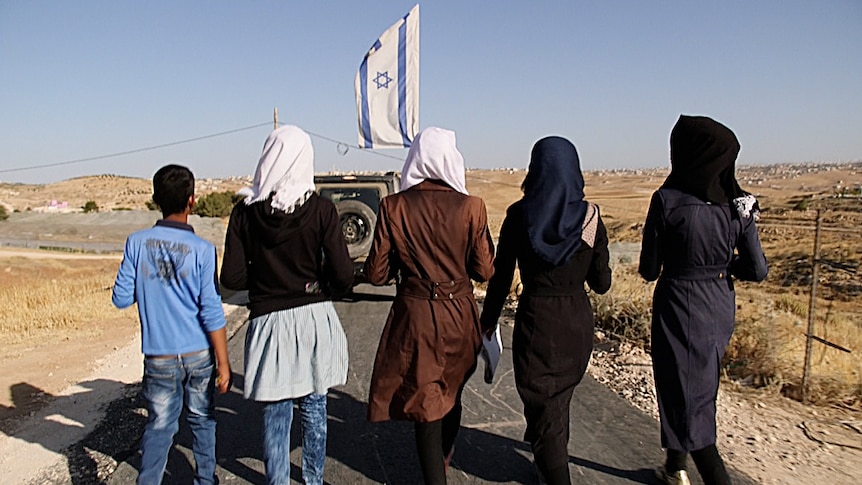 Four teenagers from the village of Tuba walk to school accompanied by an armoured vehicle.