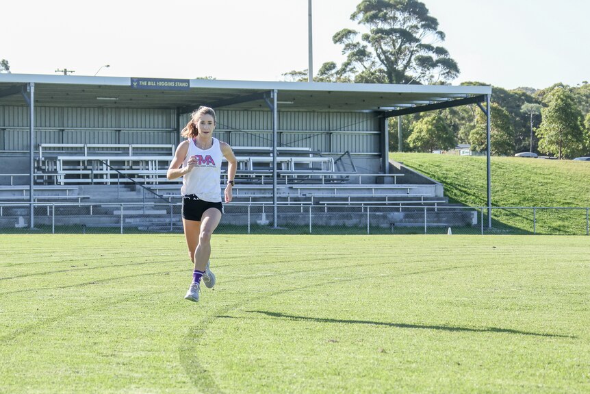 Amy O'Halloran is mid stride on a grassed running track.