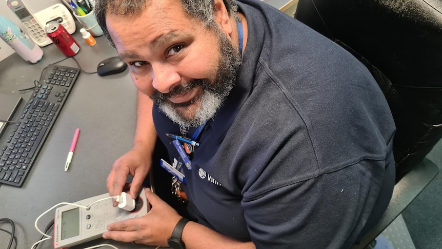 A man smiles at the camera while testing and tagging an electrical good item. 