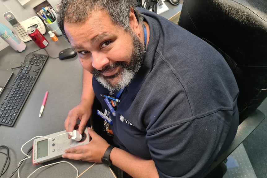 A man smiles at the camera while testing and tagging an electrical good item. 