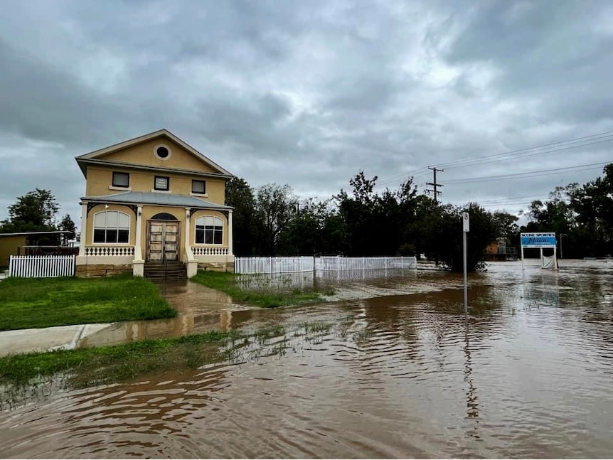 A flooded street in a country town, presided over by a rather grand two-storey, Federation-style home.