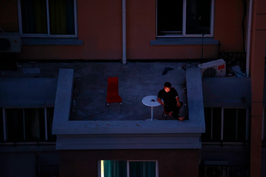 A man looks at his smartphone on a balcony in a residential community in Shanghai, China, Monday, April 11 2022. 