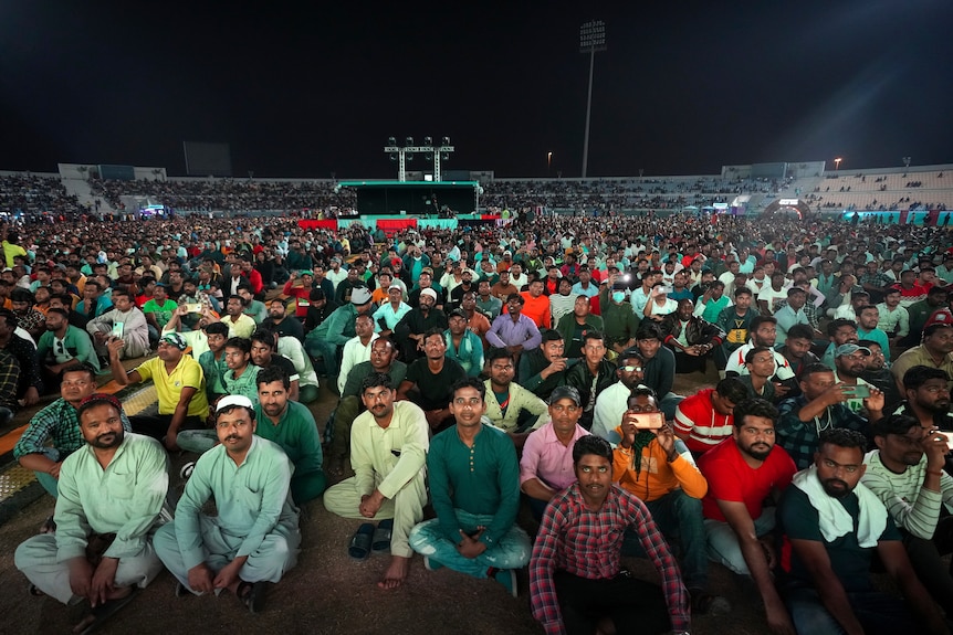 A wide shot of a large crowd sitting down in a cricket stadium watching the World Cup.