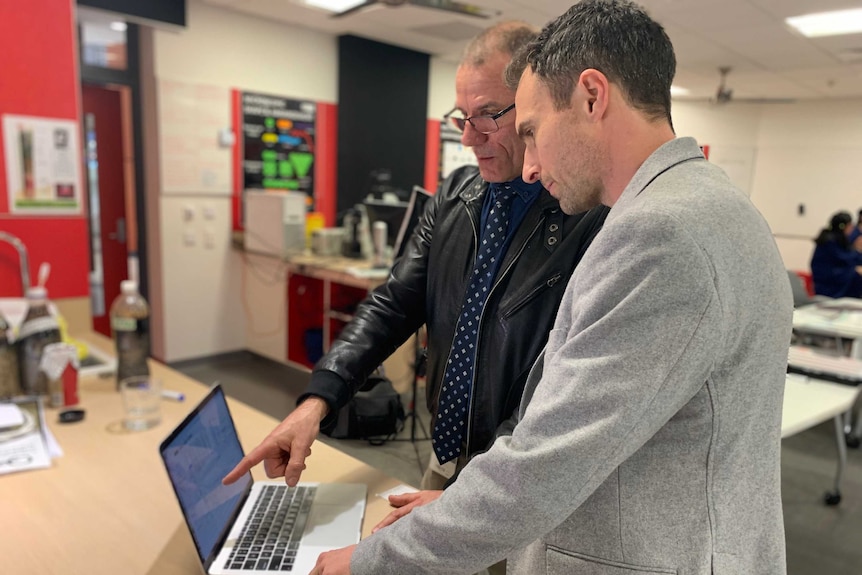 Two men look at a computer in a classroom.