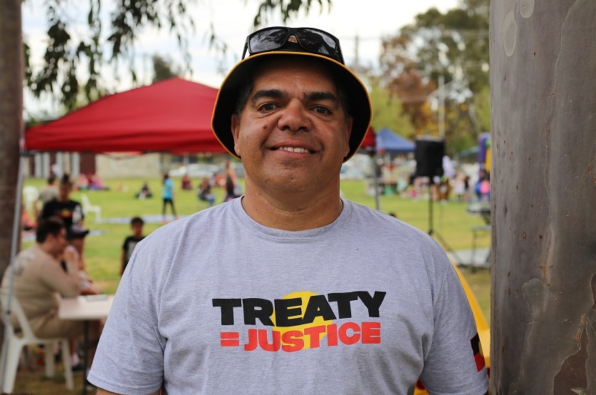 Graham Briggs is dressed in a 'Treaty = Justice' t-shrit as he stands, smiling, next to a gum tree.