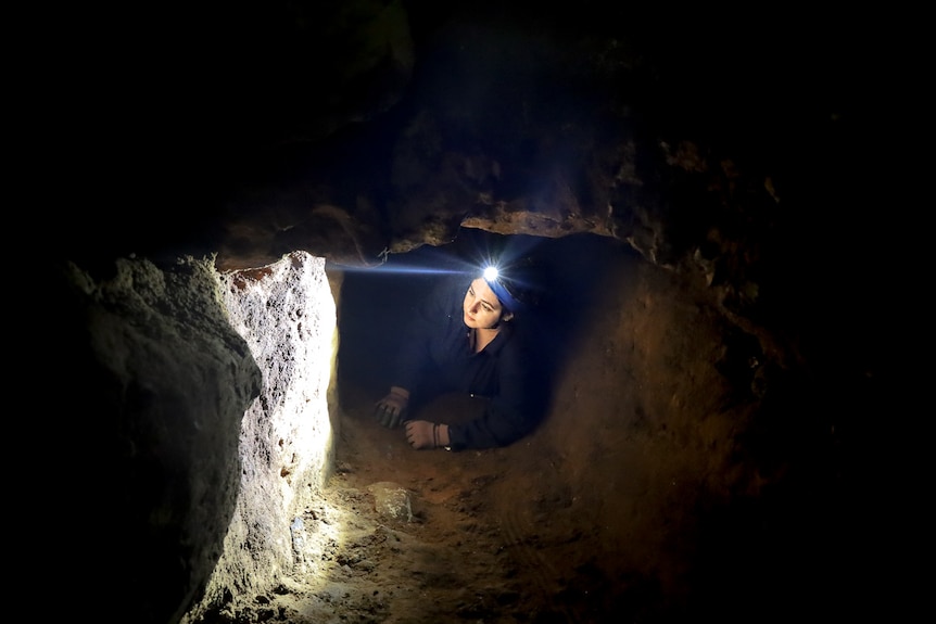 A woman crawls through a tunnel with a headtorch