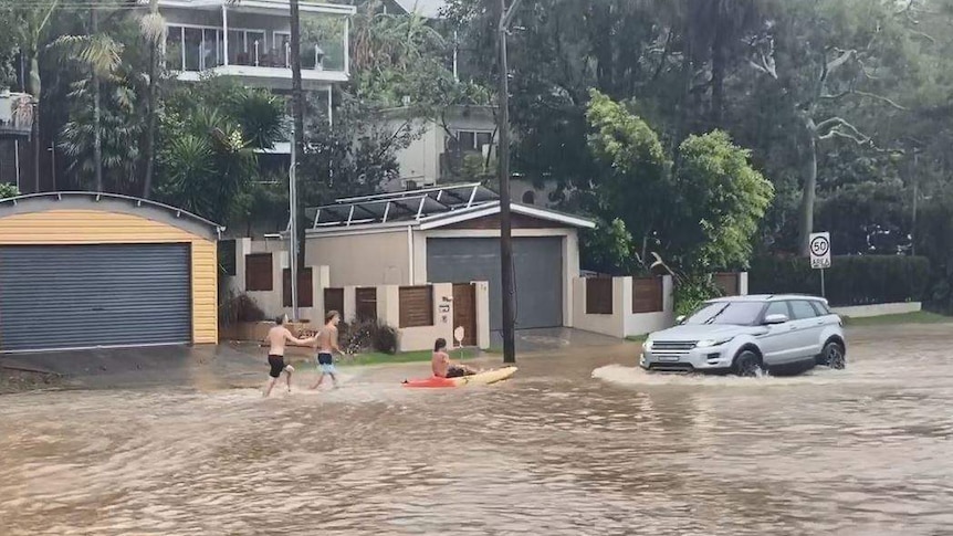 Three kids with a kayak and a four wheel drive on a flooded suburban street.