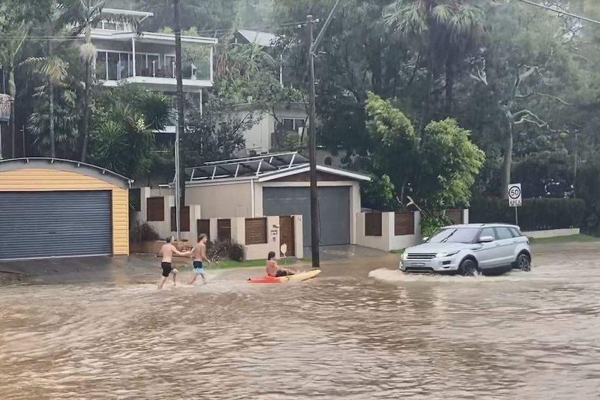 Three kids with a kayak and a four wheel drive on a flooded suburban street.