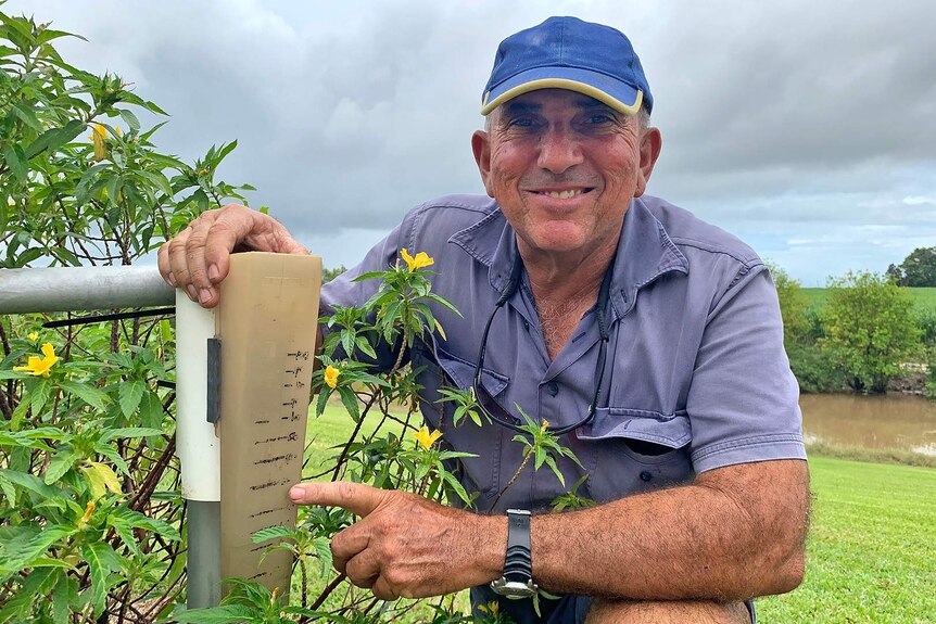 Cane farmer Paul Mizzi squats down beside his rain gauge which looks quite old.