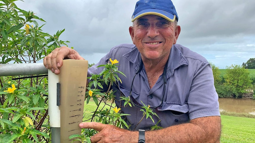 Cane farmer Paul Mizzi squats down beside his rain gauge which looks quite old.