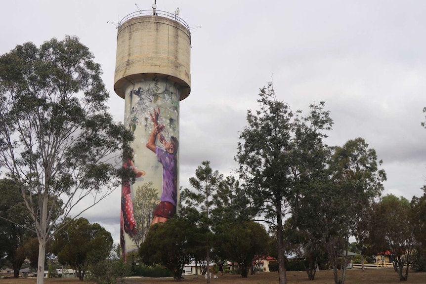 A water tower covered in a mural of children and surrounded by trees
