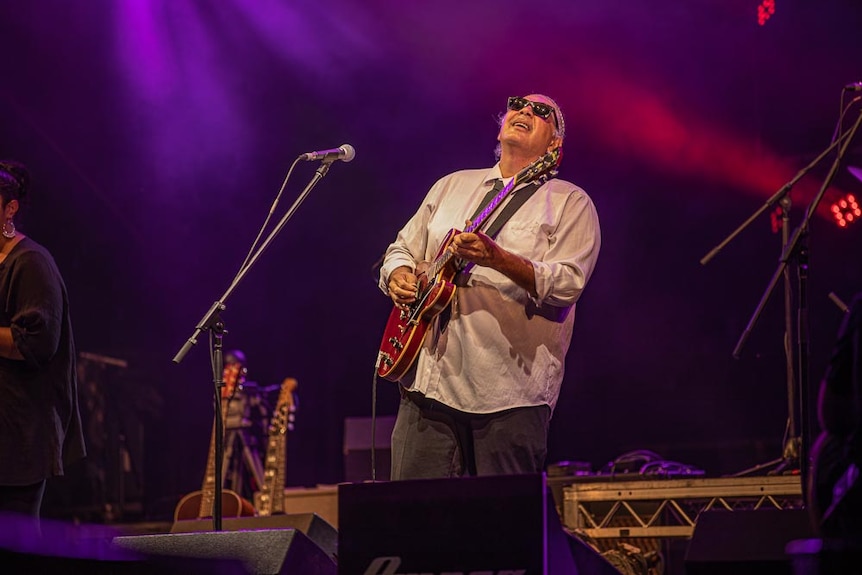 A man plays a blues guitar on a music festival stage.