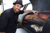 Justin Whitrow stands next to a barbeque grilling crocodile