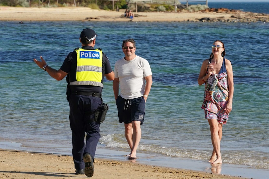 A police officer speaks to a man and a woman at the beach on a sunny day.