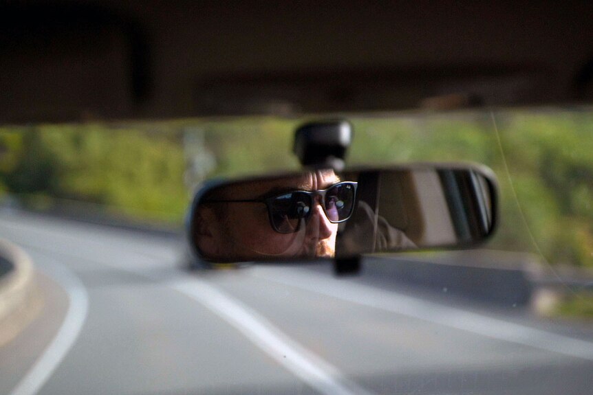 the reflection of a man wearing sunglasses in a rear view mirror