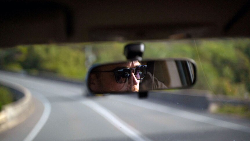 the reflection of a man wearing sunglasses in a rear view mirror