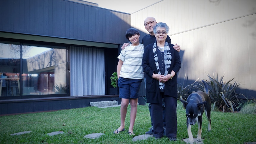 Three family members stand in front of their house