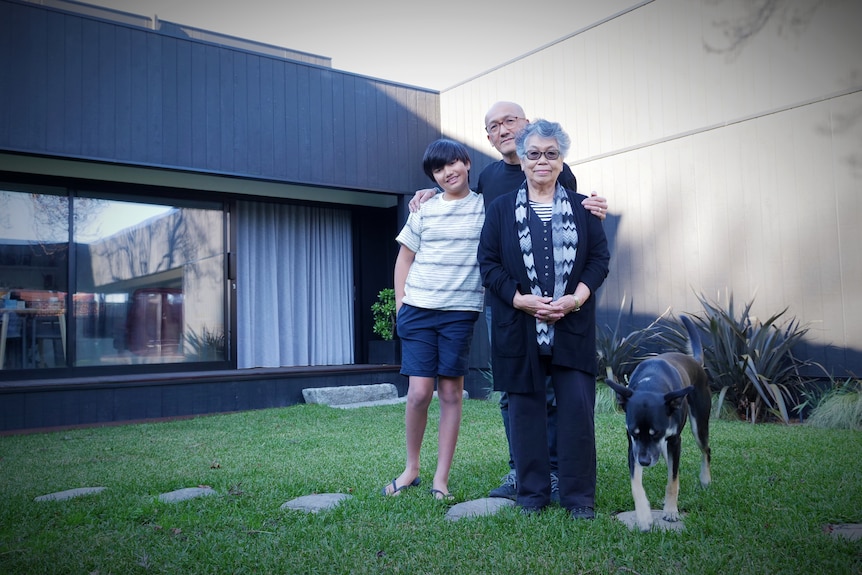 Three family members stand in front of their house