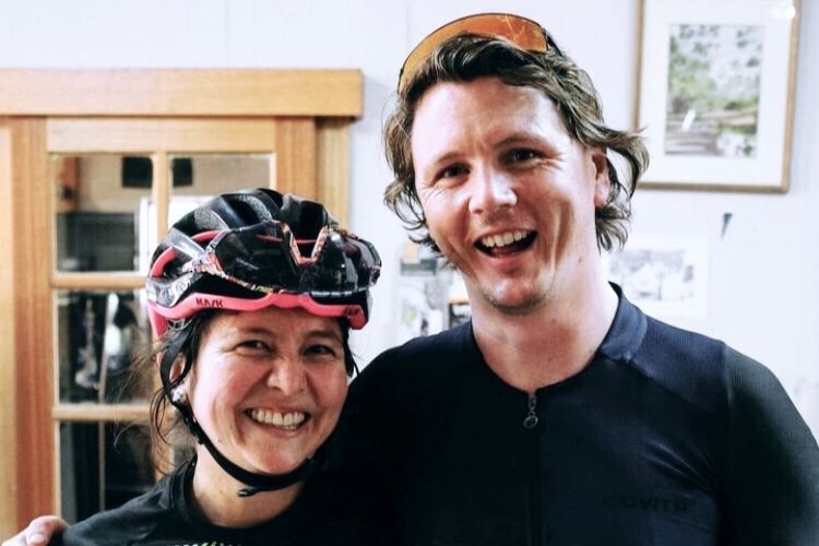 A woman wearing cycling clothing and a helmet smiling, standing next to a man.