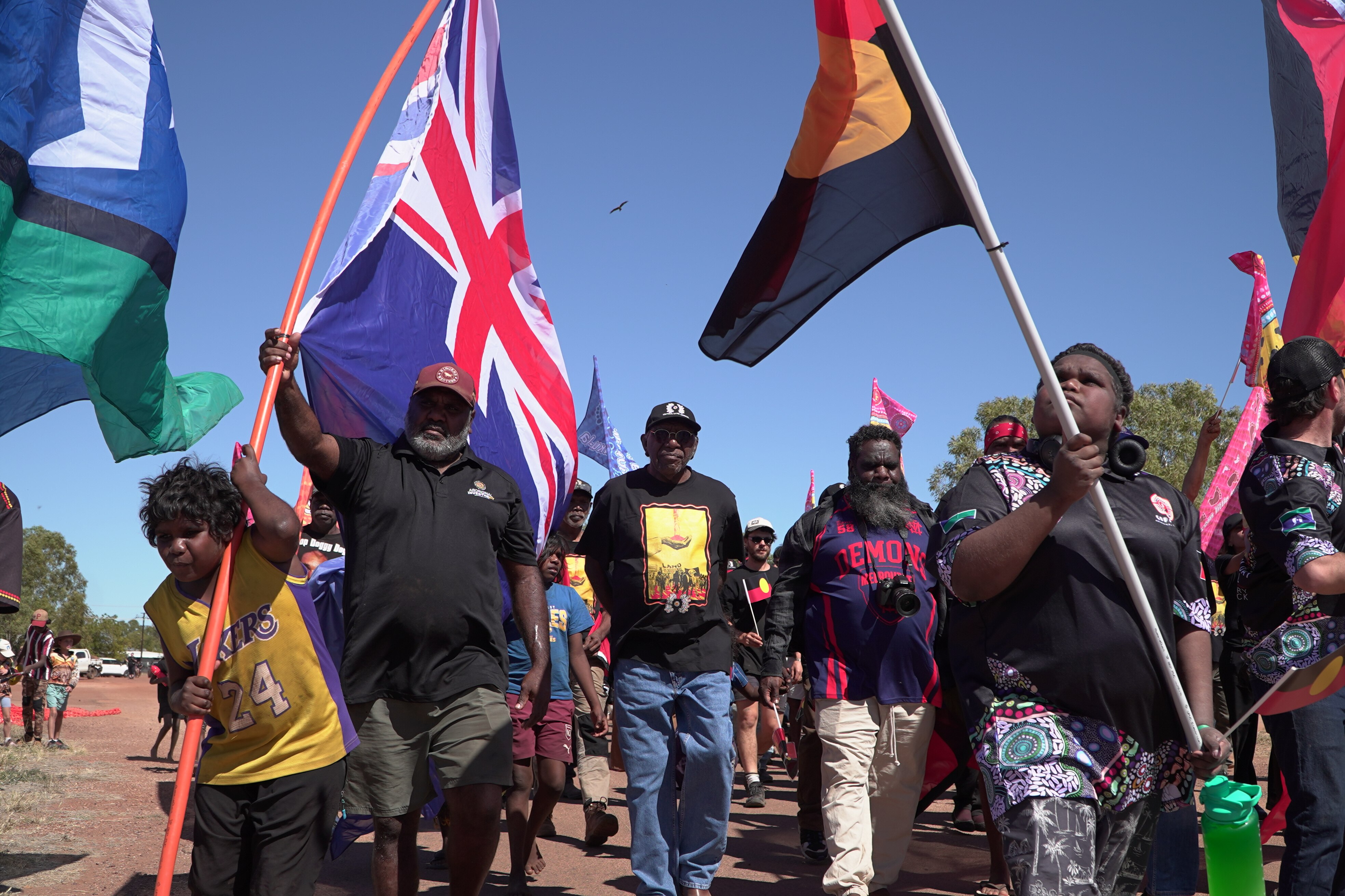 A group of Aboriginal people, young and old, marching together, holding Australian, Aboriginal and Torres Strait Islander flags.
