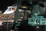 A cruise ship is seen at night behind a departing bus