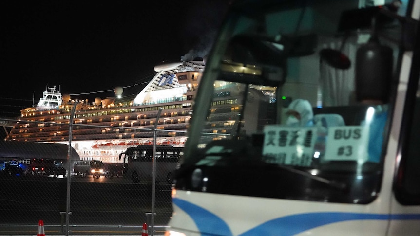 A cruise ship is seen at night behind a departing bus