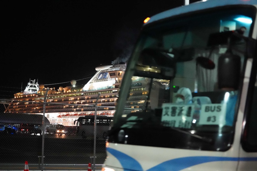 A cruise ship is seen at night behind a departing bus