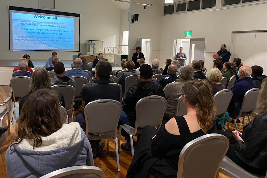 A hall full of people listening to a speaker, a screen with text on it.