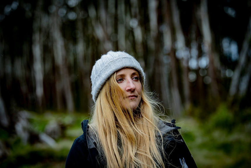 A close-up portrait shot of Dr Kita Ashamn wearing a beanie and rain jacket while standing in the forest