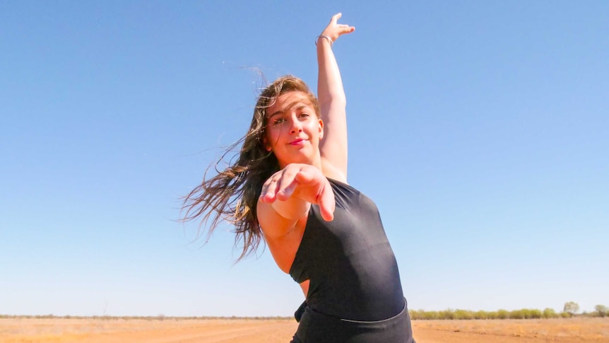 Teenager dancer Melanie Kilili stands in the red dirt dancing.