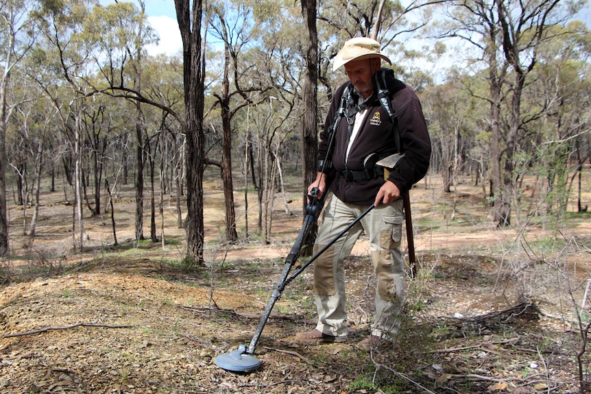 A man with a broadbrim hat mining for gold with a metal detector