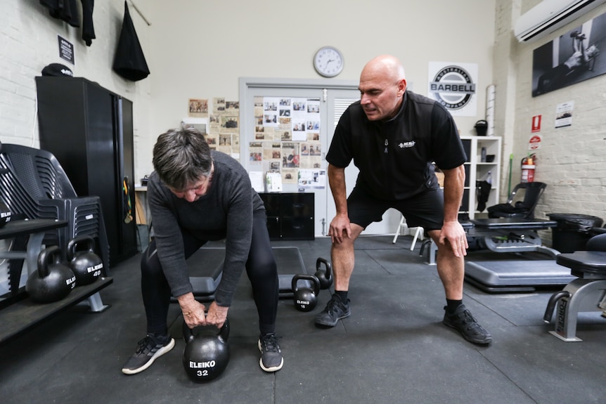 Sally Berridge lifting a Kettlebell with coach Dean Mawby beside her.