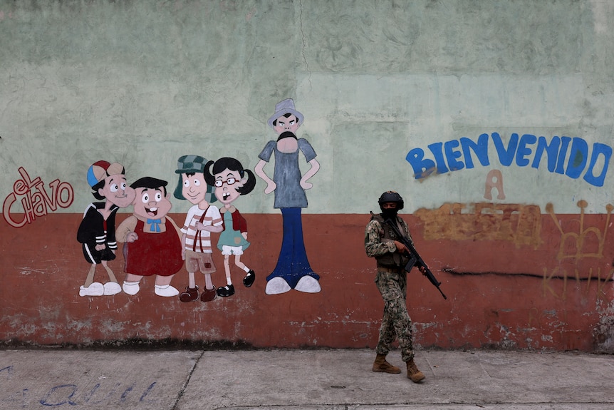 Soldier holding a rifle stands next to cartoonish graffiti 